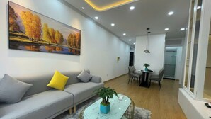 A modern living room with a grey sofa, a coffee table with a plant, and a dining area with a table and chairs. - Nam Son Luxstay SG (Ho Chi Minh City)