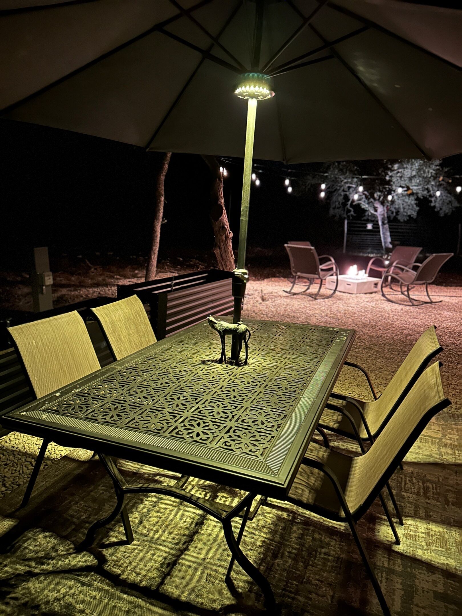 Un espace de restauration en plein air avec une table et des chaises sous une tente, entouré d’arbres et agrémenté d’un foyer.