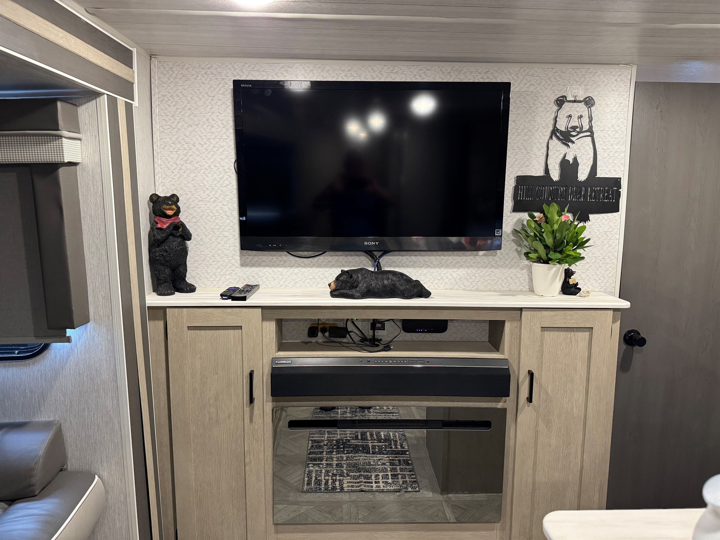 Un salon moderne avec un téléviseur à écran plat fixé au-dessus d’un meuble en bois, une petite figurine d’ours et une plante en pot.