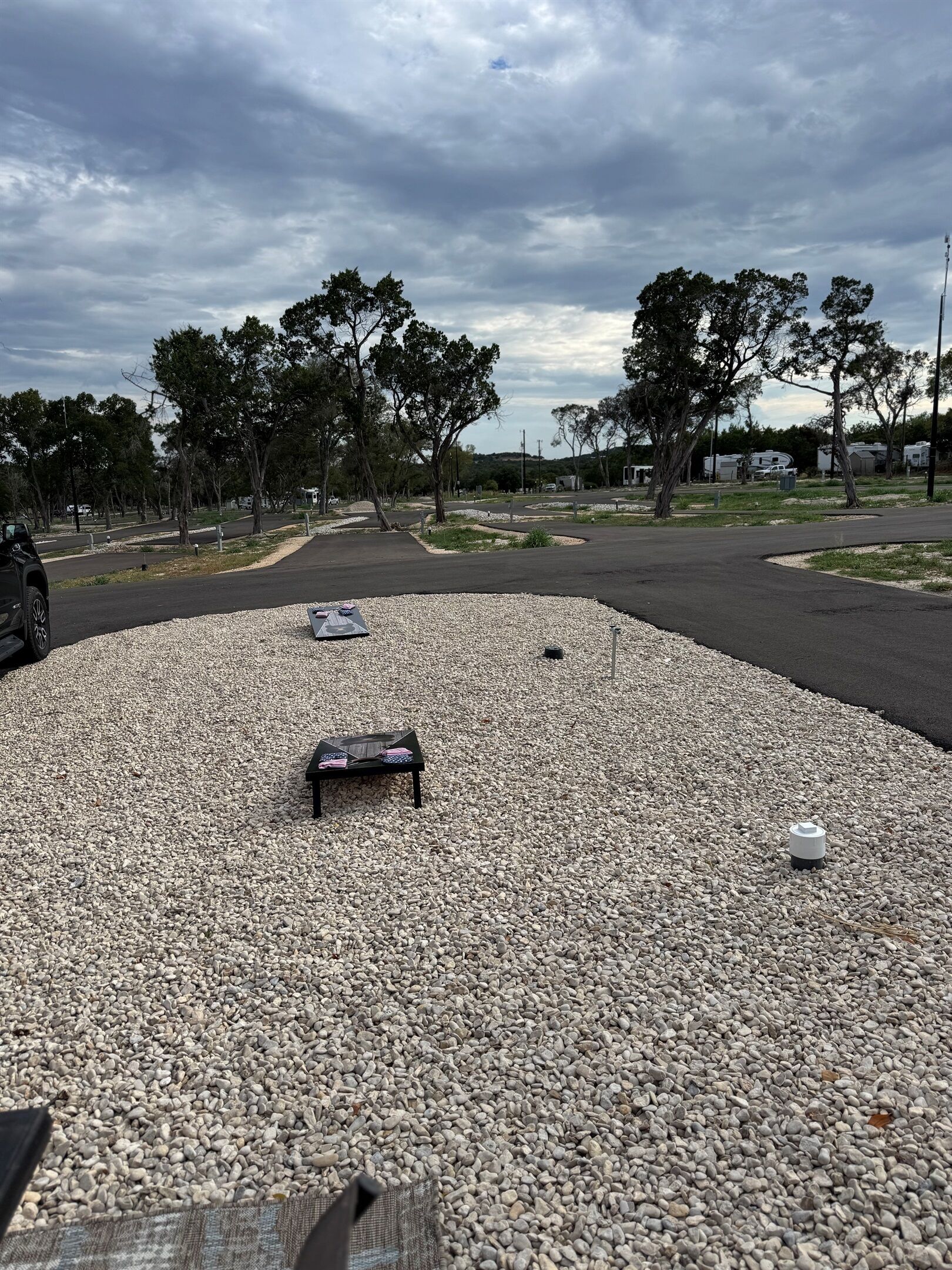A gravel area with a small table and a chair, surrounded by trees and a road.