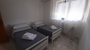 A small, clean room with two single beds, a radiator, and a window with blinds. - An oasis of tranquility in a strategic location, "Belvedere da Madia "in Monopoli. (Monopoli)