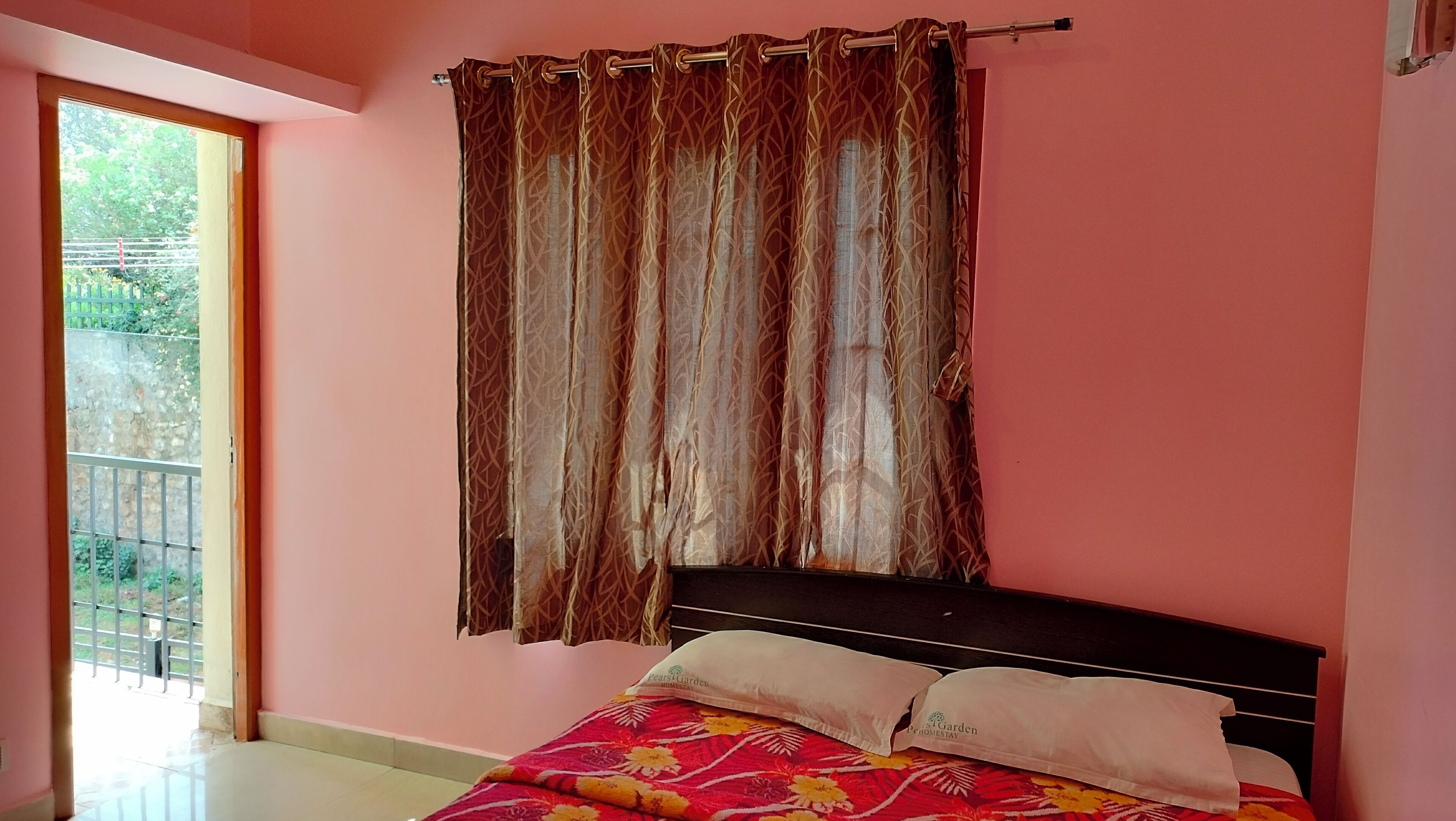 A bedroom with a bed, a window with a view of greenery, and a curtain.