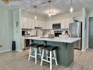 A modern kitchen with a central island, bar stools, stainless steel appliances, and pendant lighting. - Sea Oats C203 2 bedroom / 2 bathroom  pet friendly Complete remodel (Gulf Shores)