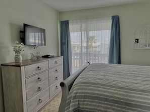 A bedroom with a bed, a dresser with drawers, a television on the wall, and a window with curtains. - Sea Oats C203 2 bedroom / 2 bathroom  pet friendly Complete remodel (Gulf Shores)