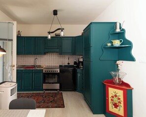 Une cuisine de taille réduite avec des meubles de couleur turquoise, une cuisinière à gaz, un lave-vaisselle et une machine à café.