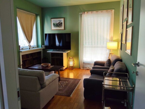 Un salon avec un canapé, un téléviseur, une lampe et une fenêtre avec des rideaux.