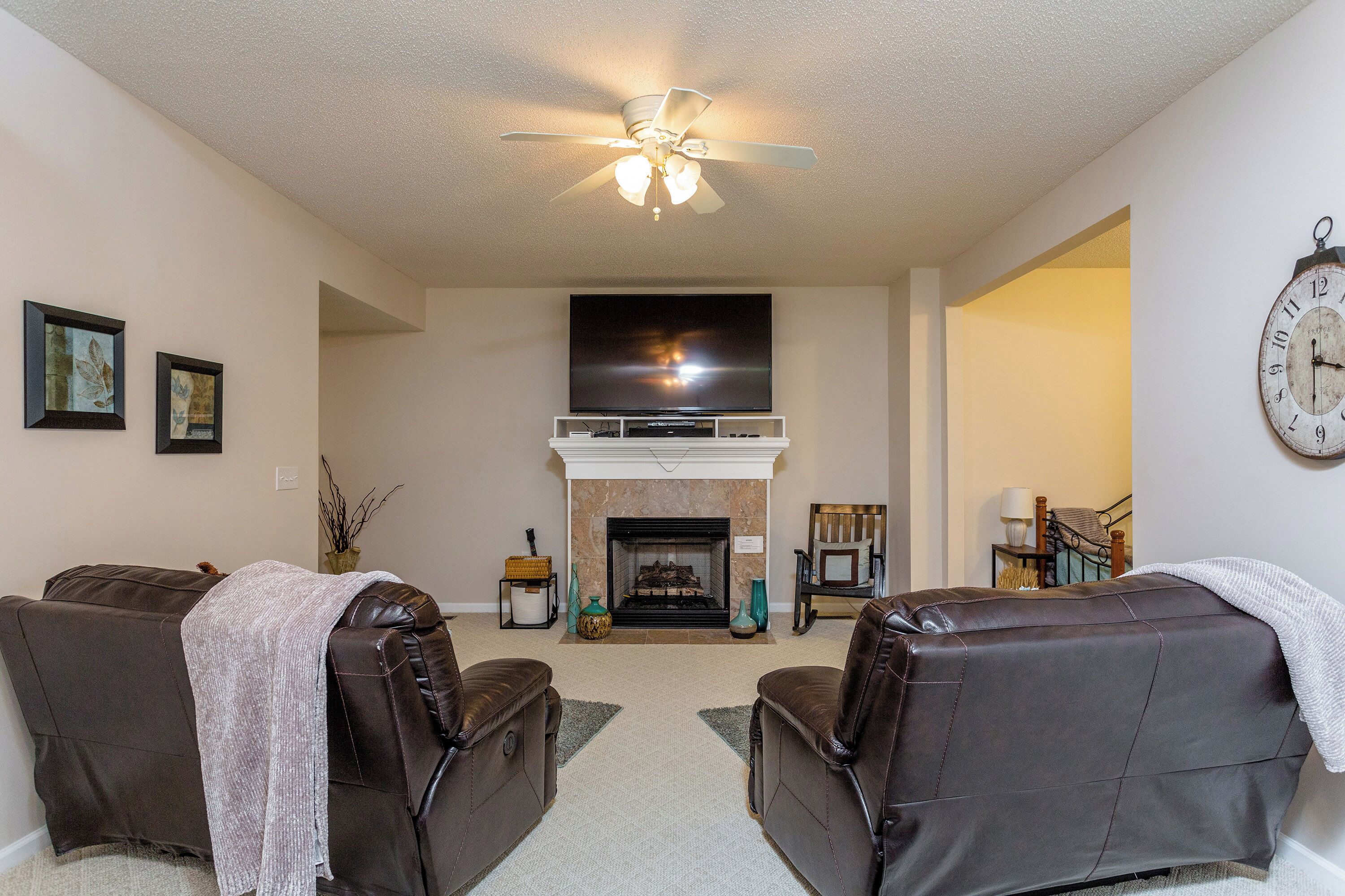 A living room with two leather sofas, a fireplace, a television, and a clock on the wall.