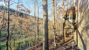 A wooden deck attached to a house with a view of a forested area and a distant hill.