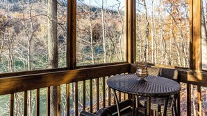 A wooden deck with a wicker table and chairs, overlooking a forested area.