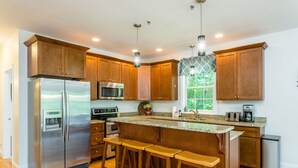 A modern kitchen with wooden cabinets, stainless steel appliances, a granite countertop, and bar stools. - Sunrise Views & Mountain Charm! (Mc Gaheysville)