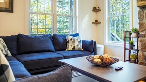 A living room with a dark blue sofa, a coffee table with a basket of snacks, and a stone accent wall. - Sunrise Views & Mountain Charm! (Mc Gaheysville)