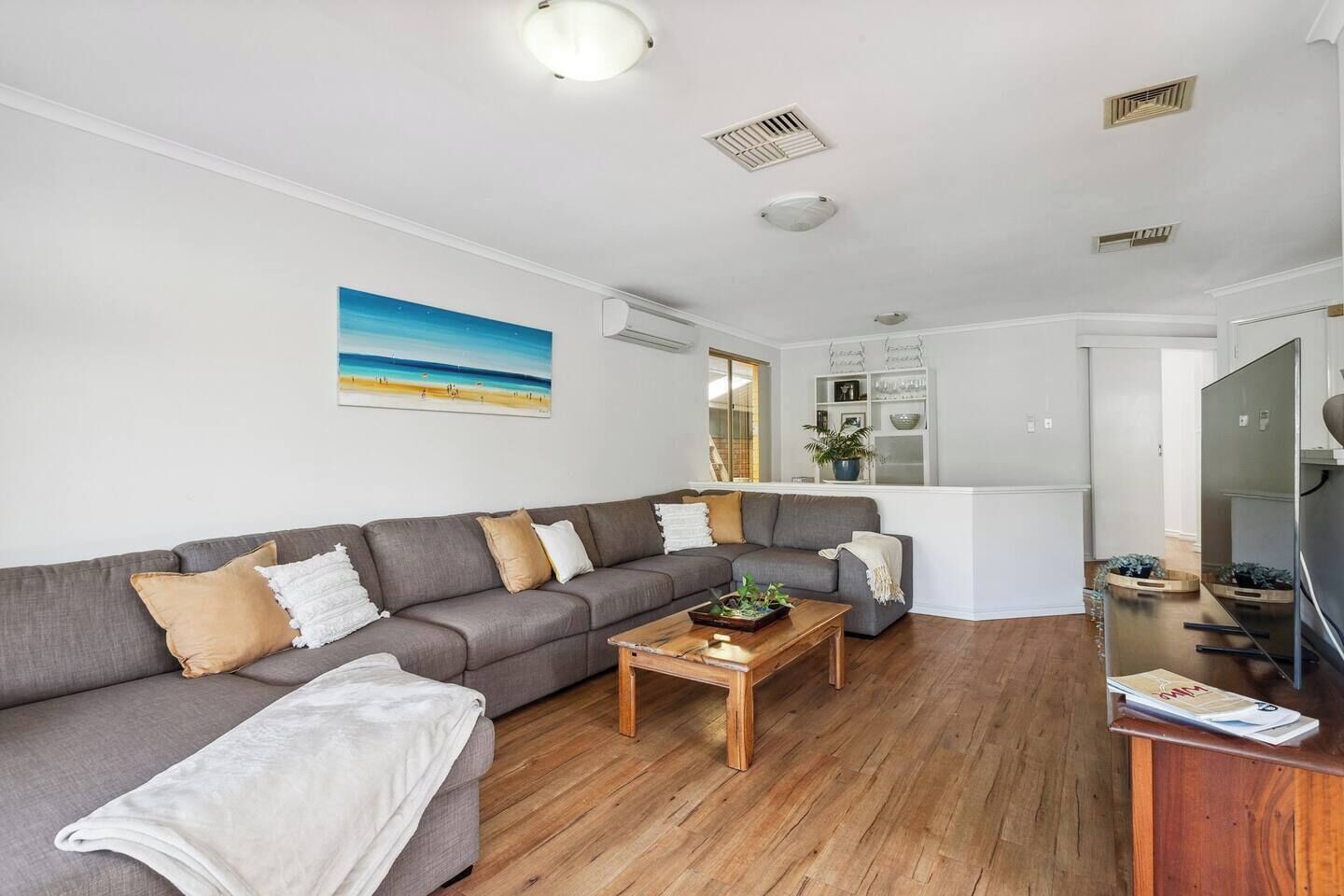Uma sala de estar moderna com um sofá modular cinza, uma mesa de centro de madeira e uma televisão de tela plana.