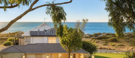 A coastal house with a tiled roof, solar panels, and a view of the sea.