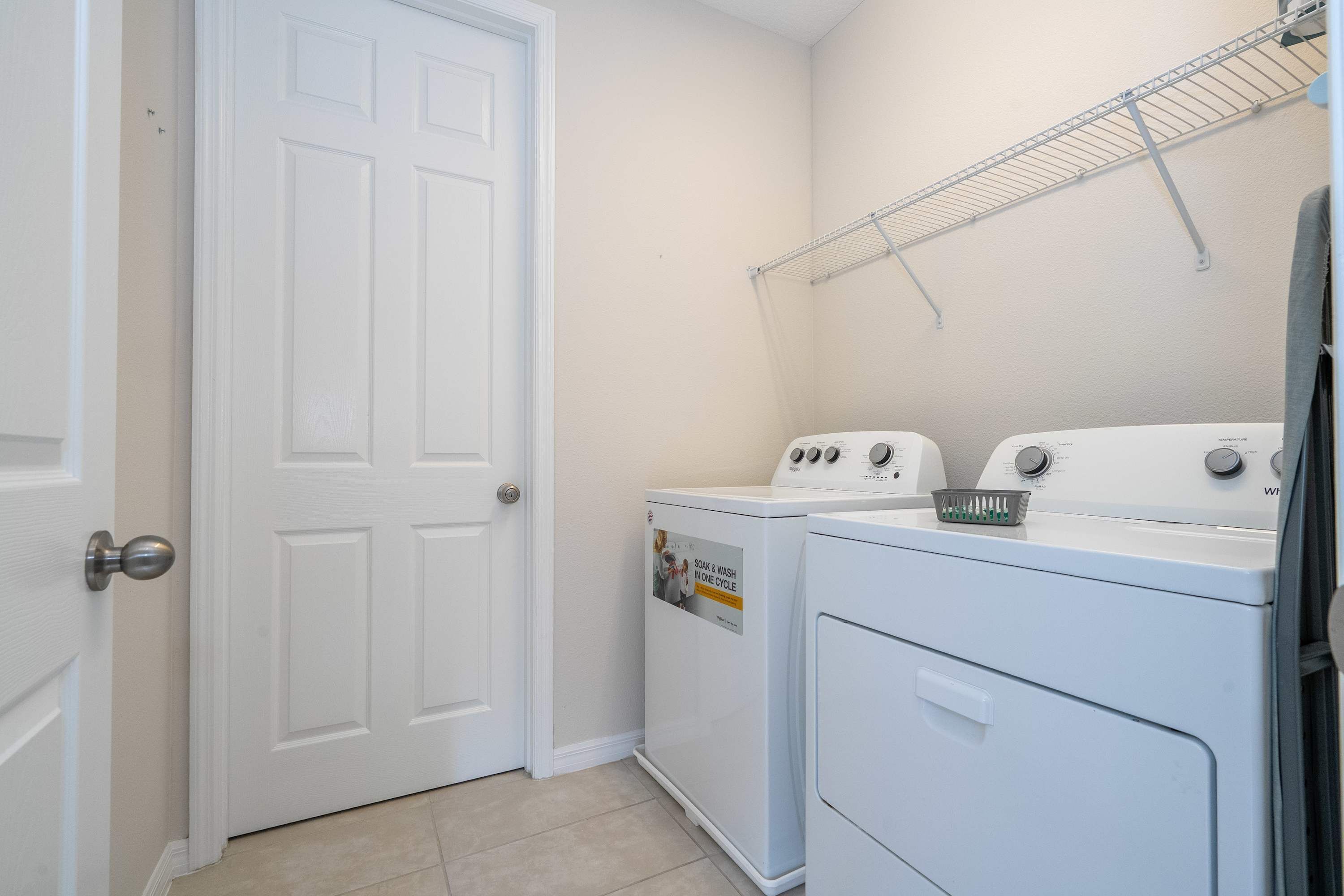 A laundry room with two stacked washers and dryers, a metal drying rack, and a white door.
