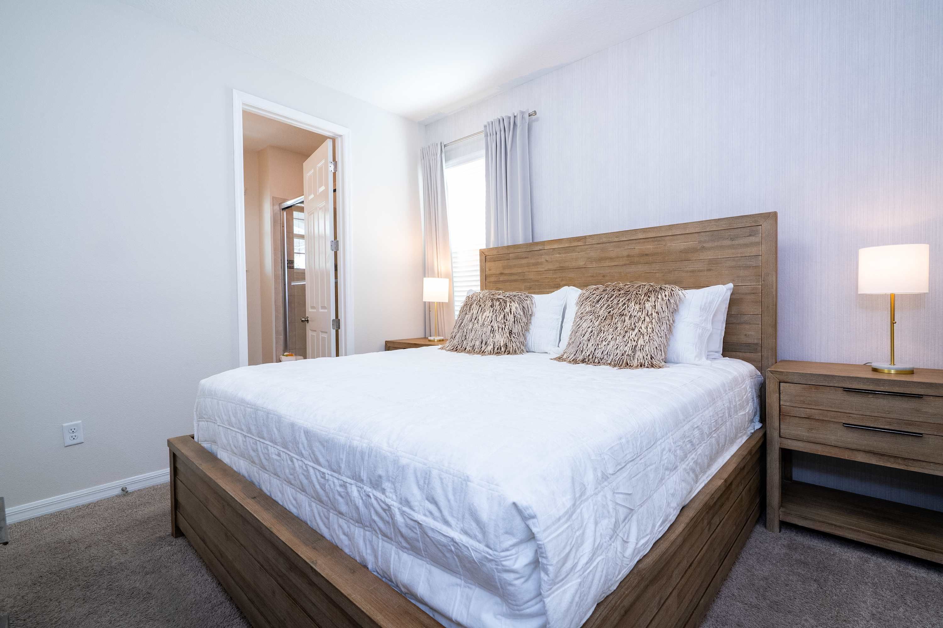 A bedroom with a wooden bed frame, white bedding, and two bedside tables with lamps.