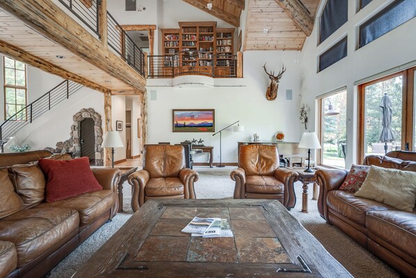 A spacious living room with leather sofas, a coffee table, and a large wooden staircase.
