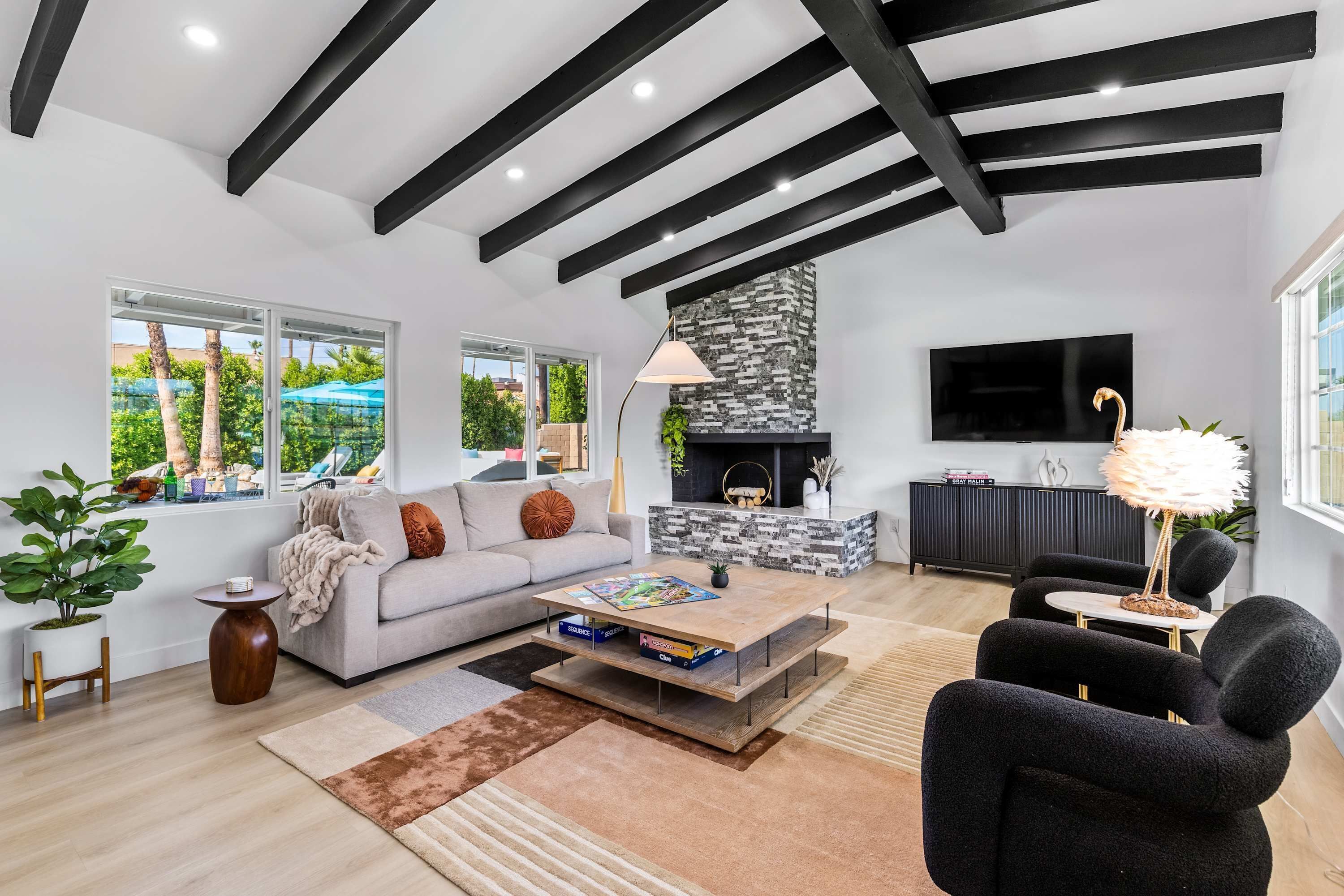 A modern living room with a sofa, coffee table, and black armchairs. There is a fireplace, a television, and a large window with a view of greenery.