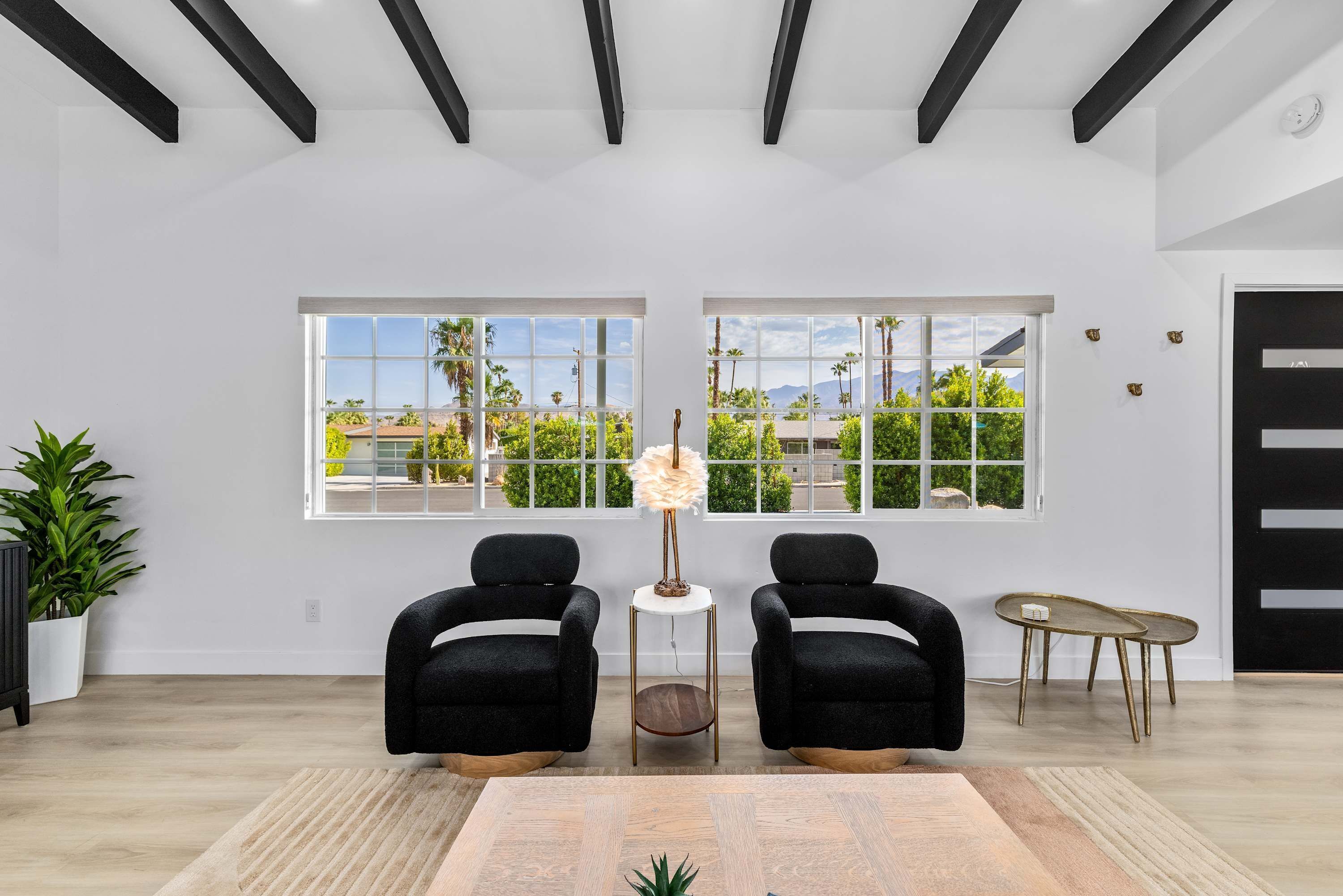 Una habitación amplia con dos sillones negros, una pequeña mesa redonda y un ventanal que ofrece vistas a zonas verdes y edificios.