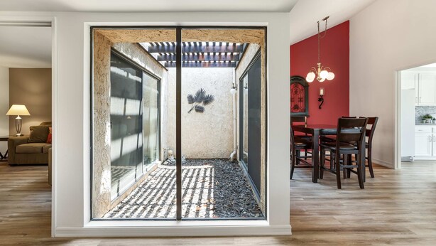 Un intérieur moderne avec une cloison en verre, un coin repas avec des chaises en bois et un mur d’accent rouge.
