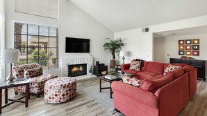 Un salon moderne avec une cheminée, un canapé rouge, des poufs à motifs et un téléviseur à écran plat.