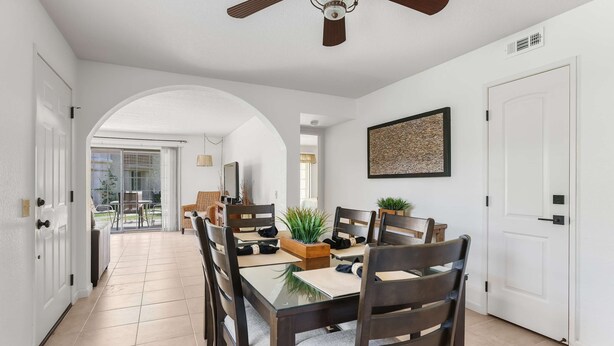 A dining area with a glass table, dark wooden chairs, and a ceiling fan. - 2BR 2BA Stylish Palm Springs Condo (Palm Springs)