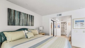A bedroom with a large bed, a nightstand, a wall-mounted lamp, and a door leading to a bathroom. - 2BR 2BA Stylish Palm Springs Condo (Palm Springs)
