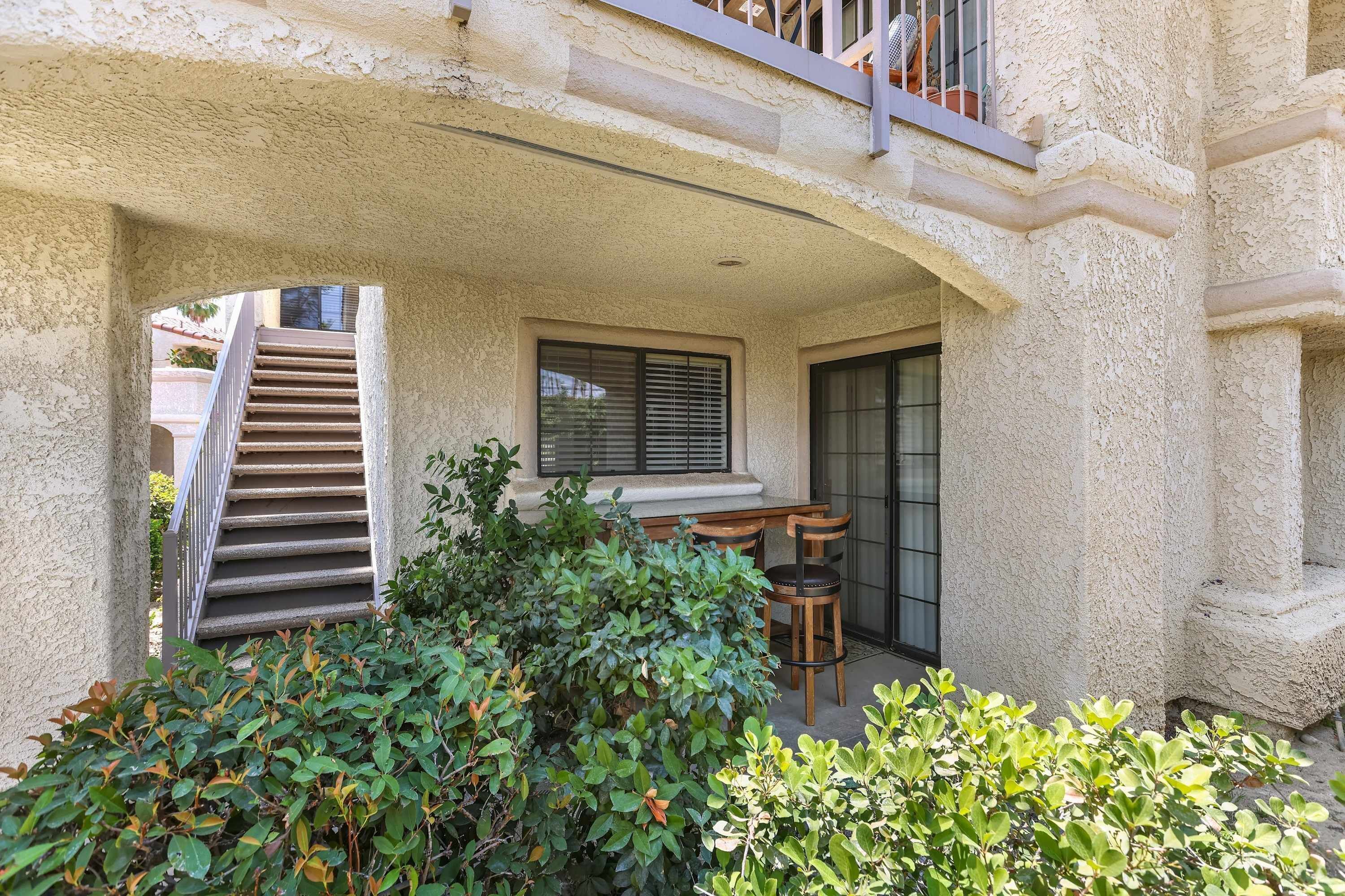 A covered outdoor area with a staircase, a window with blinds, and a table with chairs.