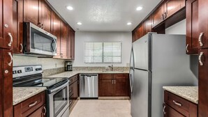A kitchen with wooden cabinets, stainless steel appliances, granite countertops, and a window with blinds. - 2BR 2BA Stylish Palm Springs Condo (Palm Springs)