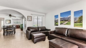 A spacious living room with a brown leather sectional sofa, a dining area with a table and chairs, and a kitchen in the background. - 2BR 2BA Stylish Palm Springs Condo (Palm Springs)