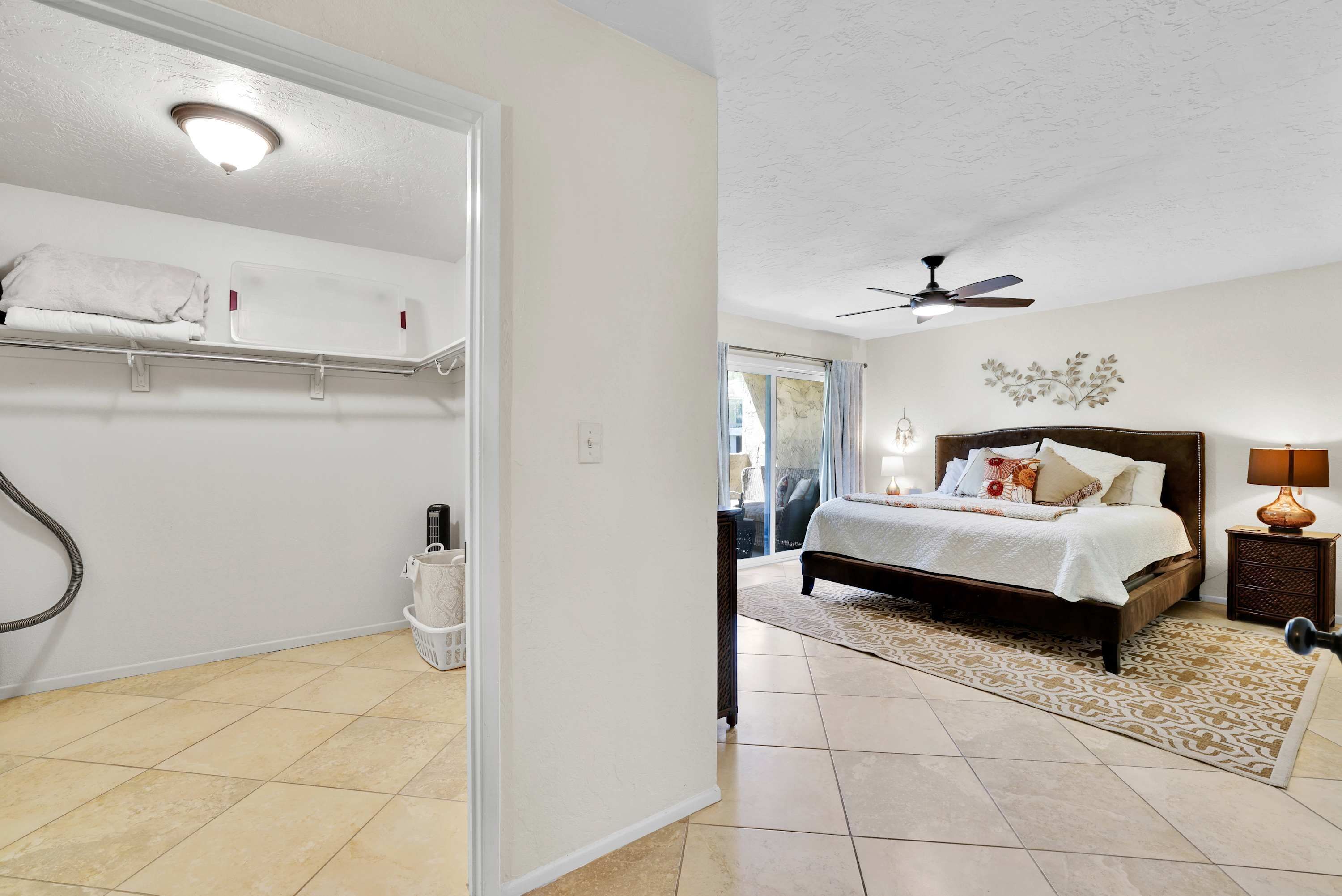 A bedroom with a bed, a nightstand, a lamp, a ceiling fan, and a view of the outside.