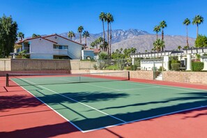 A tennis court with a net, surrounded by a brick wall and palm trees, with a mountain in the background. - Stylish Condo With Panoramic View Community Pool (Palm Springs)