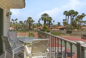A balcony with outdoor seating, a tennis court, and palm trees in the background. - Stylish Condo With Panoramic View Community Pool (Palm Springs)