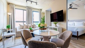 Quarto de hotel moderno com sofá, duas poltronas, mesa redonda, televisão e cama.