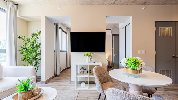 Uma sala de estar moderna com televisão de tela plana, assentos confortáveis, uma mesa de centro redonda e um vaso de planta.