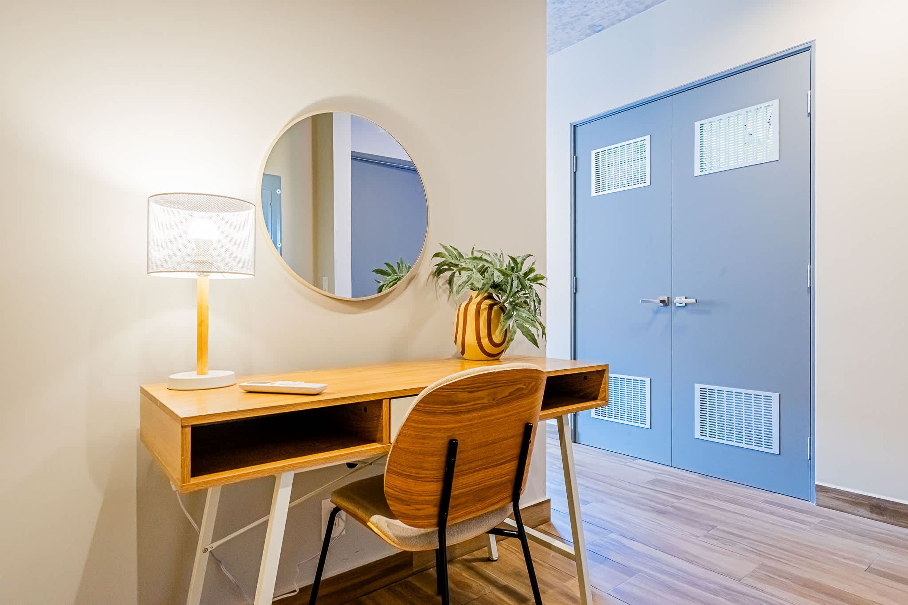 A wooden desk with a lamp, a chair, a mirror, and a potted plant.