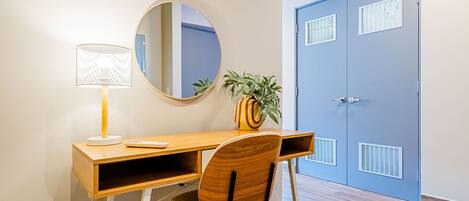 A wooden desk with a lamp, a chair, a mirror, and a potted plant.