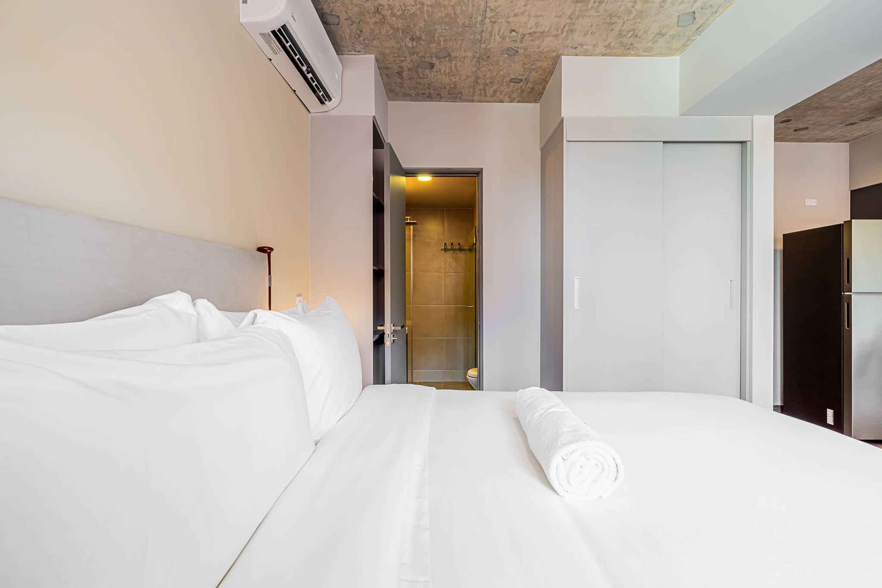 A hotel room with a large bed, a bathroom visible through an open door, and a modern ceiling design.