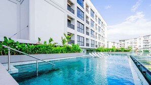 Piscina com grade de metal, rodeada por vegetação exuberante e um edifício moderno com varandas.