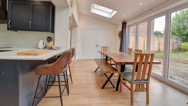 A modern kitchen with dark cabinets, a wooden island, and a dining area with a large table and chairs. - Spacious 4 bedroom house in Bishop's Stortford (Hertfordshire)
