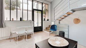 A modern living room with a glass staircase, white furniture, and large windows.