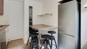 A compact kitchen with a built-in refrigerator, a wooden table, and three bar stools.