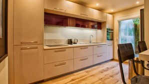 A modern kitchen with wooden cabinets, a stainless steel sink, and a dining area with a table and chairs. - Deauville Lovely Flat with Private Garden (Deauville)
