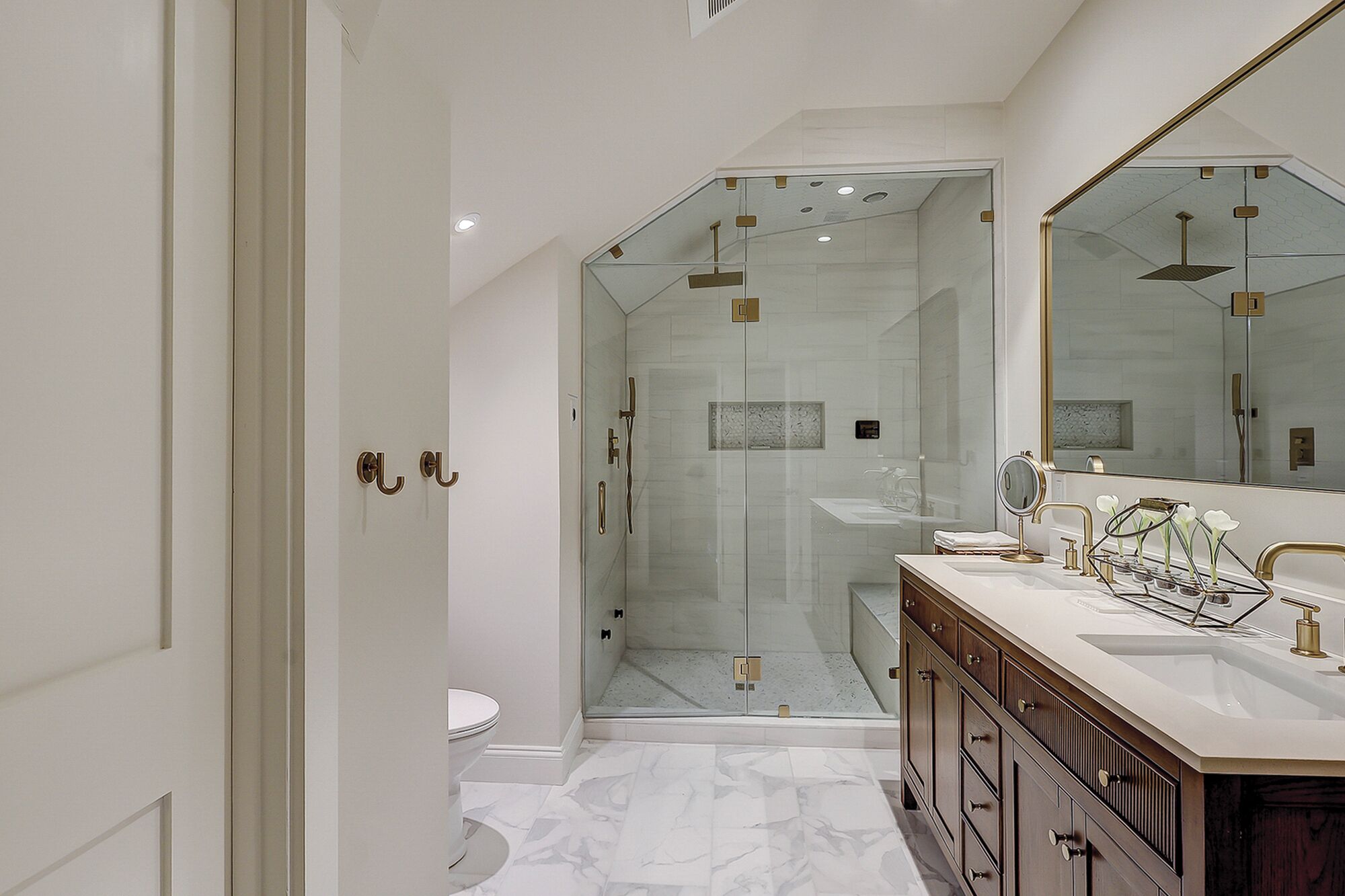 A modern bathroom with a glass-enclosed shower, a vanity with a large mirror, and marble flooring.