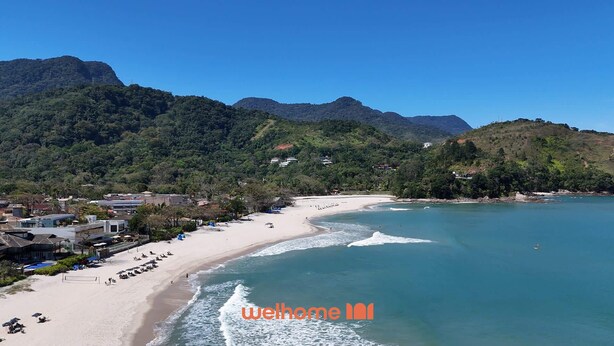 A coastal beach with clear waters, a sandy shore, and a backdrop of green hills.