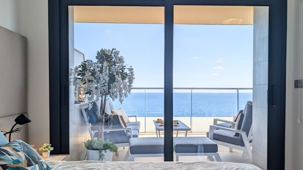 A bedroom with a large bed, a balcony with seating, and a view of the sea.