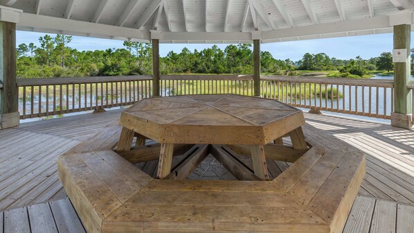 A wooden deck with a central table, surrounded by a railing, overlooking a natural landscape.