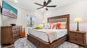 Une chambre à coucher avec un lit, des tables de chevet, une commode, un ventilateur de plafond et un téléviseur fixé au mur.