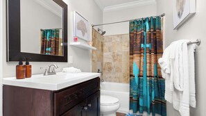 Une salle de bain avec un lavabo blanc, un meuble-lavabo en bois foncé, un grand miroir, un rideau de douche à motifs bleus et bruns, des toilettes blanches et une serviette blanche accrochée au mur.