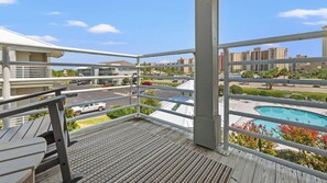 A balcony with a view of a swimming pool, a parking lot, and surrounding buildings.
