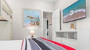 A hotel room with a bed, a TV, a painting, and a lamp.